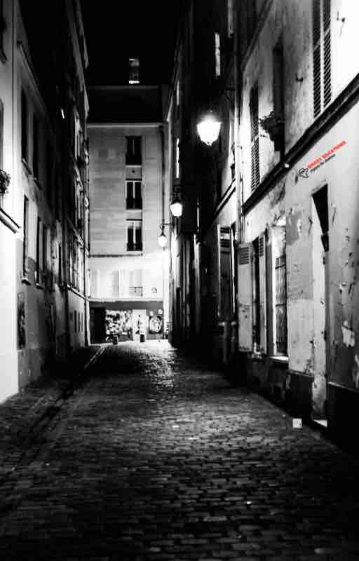 Industrial alleyway in the city illuminated by dim streetlights at night, casting eerie shadows amidst the urban landscape