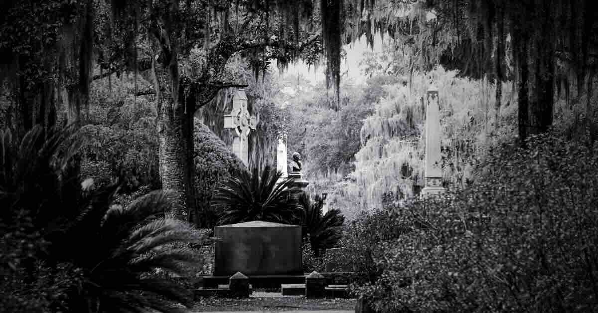 Cemetery scene featuring a historic gravestone, shrouded in mist, in front of one of the haunted hotels in Savannah GA.